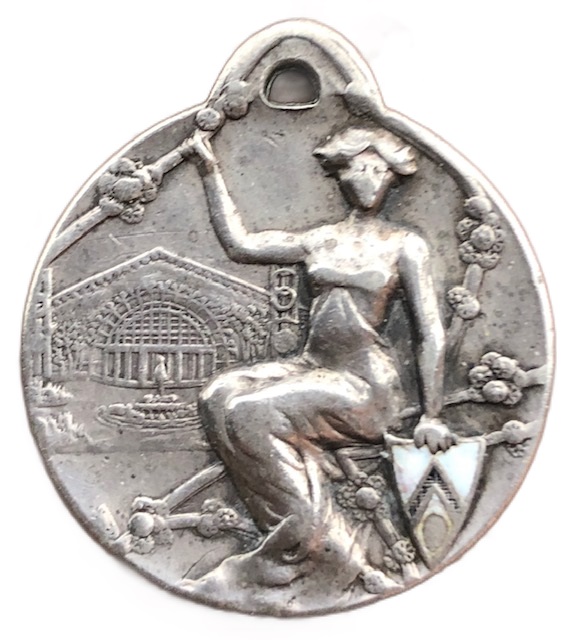 Sul dritto della medaglia, impreziosita da smalti, l'allegoria della città di Udine con stemmino smaltato e l'ingresso del padiglione principale dell'esposizione